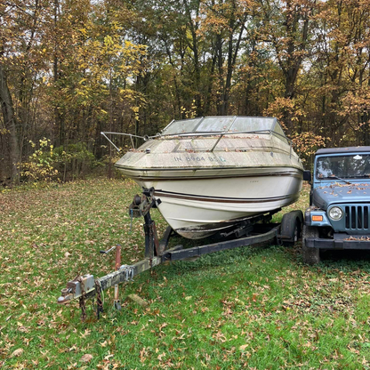 Junk boat sitting on a trailer next to a Jeep on a wooded Valparaiso property before removal by Patriot Clean Out