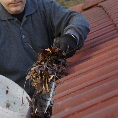 A Patriot Clean Out technician safely clearing debris from a Valparaiso home's gutters.